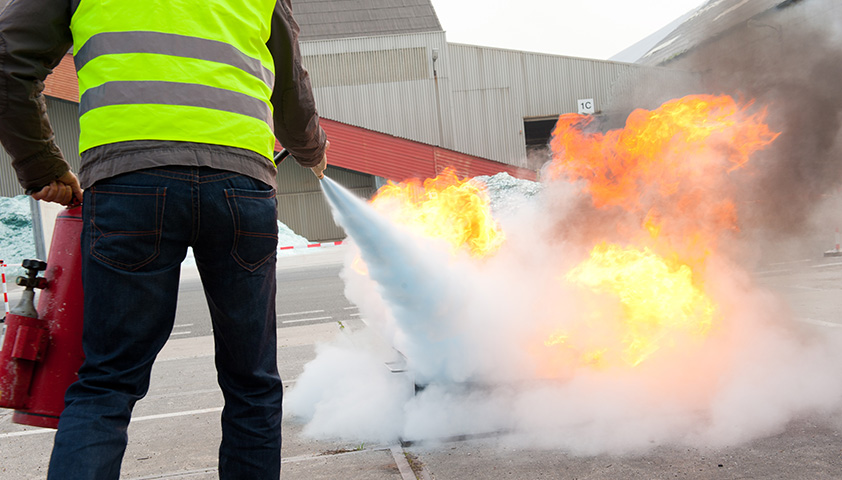 Ein Brandschutzhelfer löscht eine Flamme mit einem Feuerlöscher.